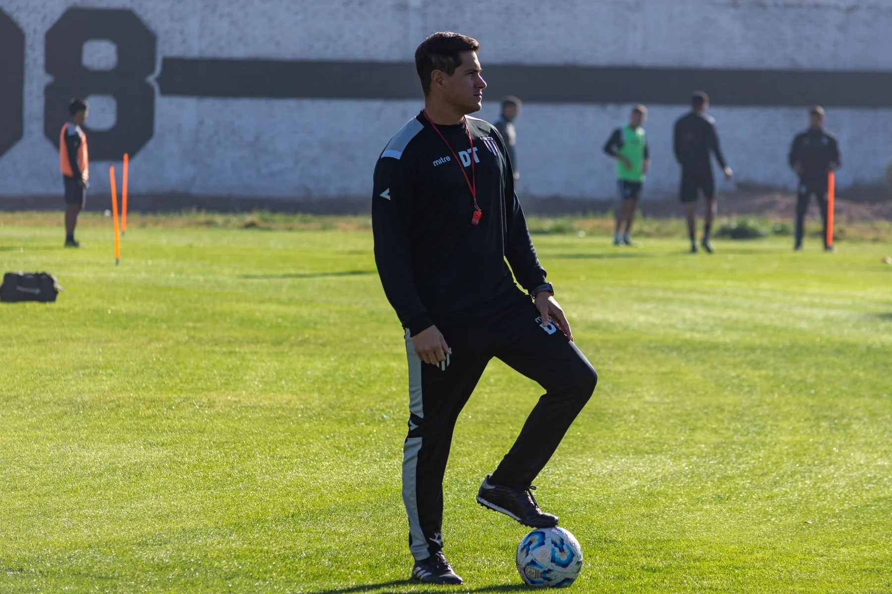 Fußballtrainer mit Ball auf dem Trainingsplatz, Spieler im Hintergrund